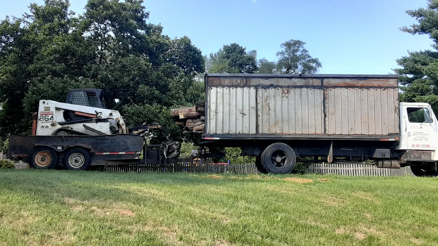 Box truck towing a skid steer on a trailer, parked on a lawn